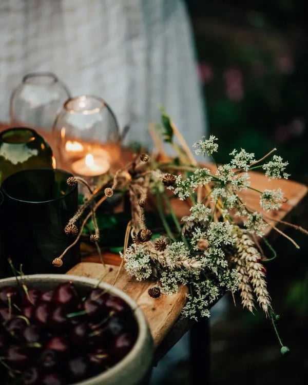 A rustic dried flower arrangement with small white blossoms, alongside glass candle domes.