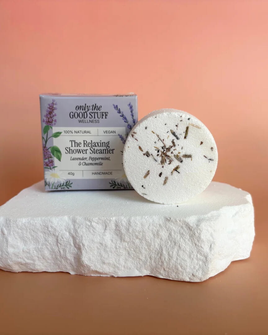A white shower steamer, with flower petals, shown next to a purple box.