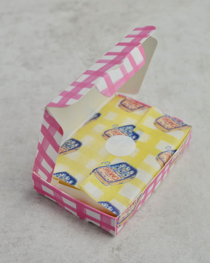 A pink and white checkered wax melt box with yellow sardine design tissue paper. 