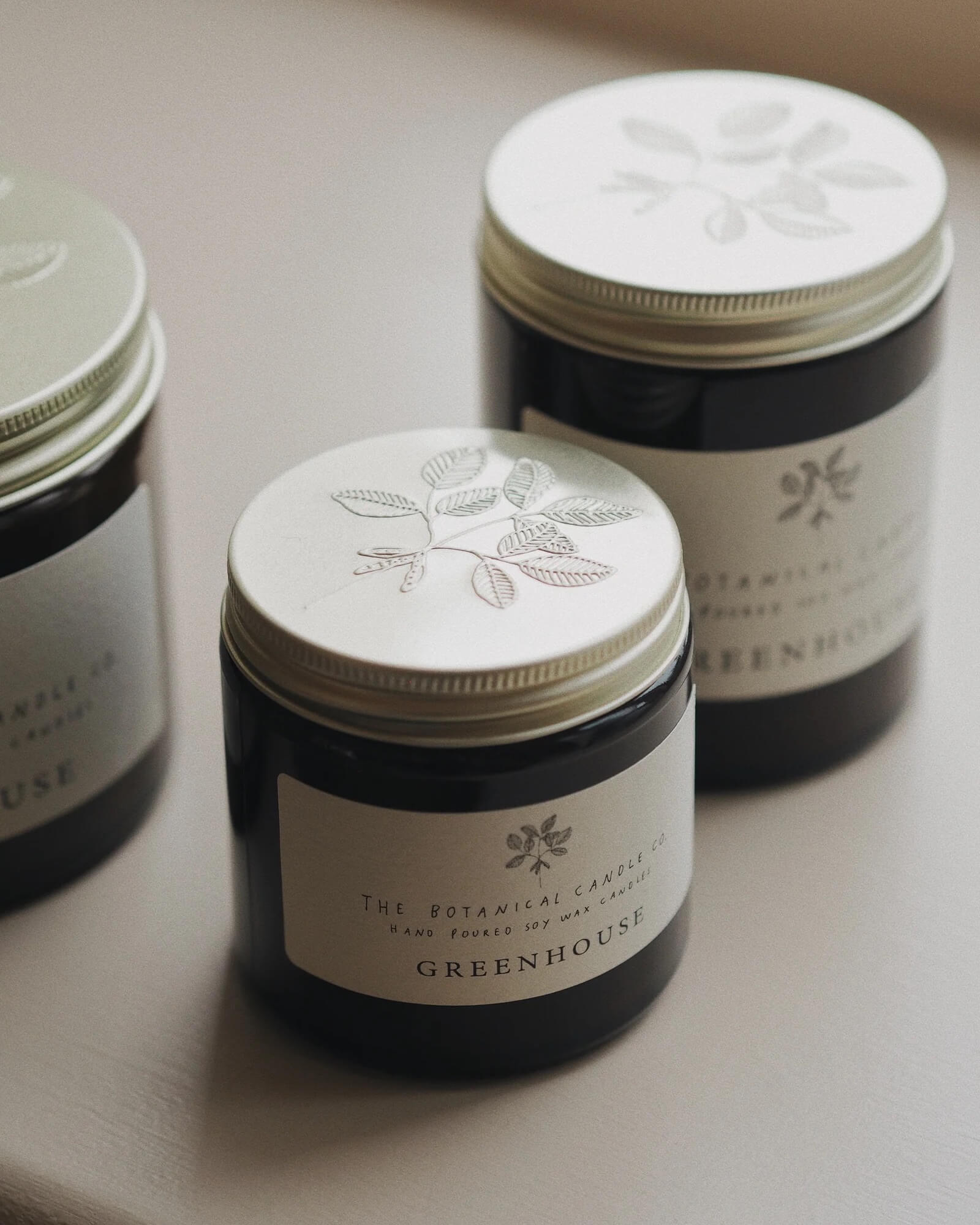 Three candles with embossed designs and labels on a light surface