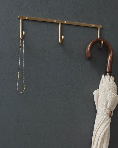 Wall-mounted brass hook with a chain and umbrella against a dark gray wall