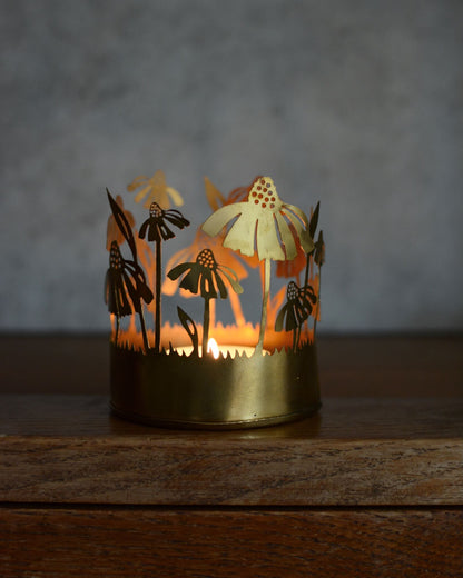 Brass tealight candle holder with floral design, illuminated by candlelight.
