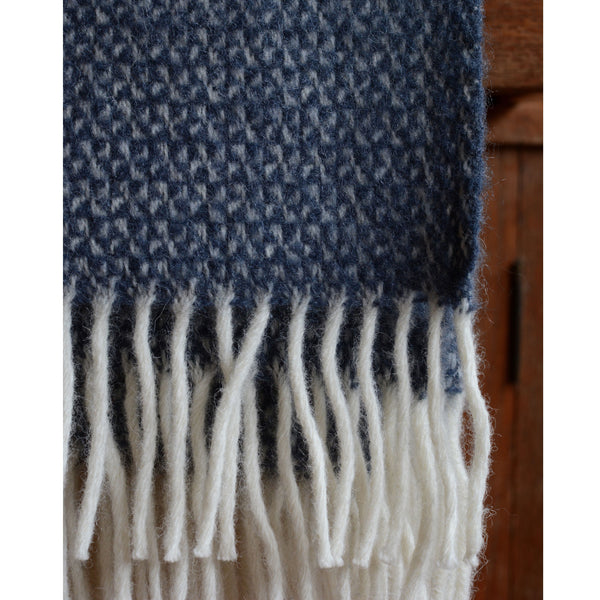 A close up of a mid blue Tweedmill windmill wool blanket with an ivory fringe.
