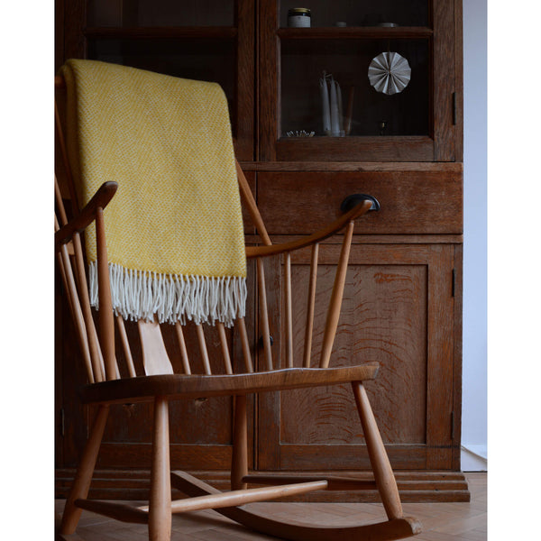 Tweedmill bright yellow beehive wool throw shown on the back of a wooden Ercol rocking chair.