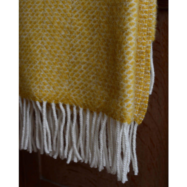 A close up photograph of a Tweedmill bright yellow beehive wool throw with ivory fringe.