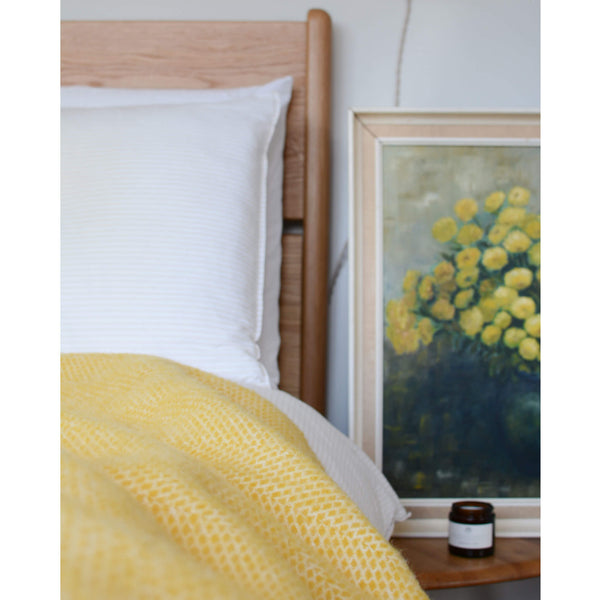 Tweedmill bright yellow beehive wool throw on a bed next to a painting of flowers..