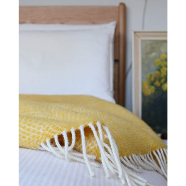 Tweedmill bright yellow beehive wool throw on a bed, showing a close up of the fringed edge.