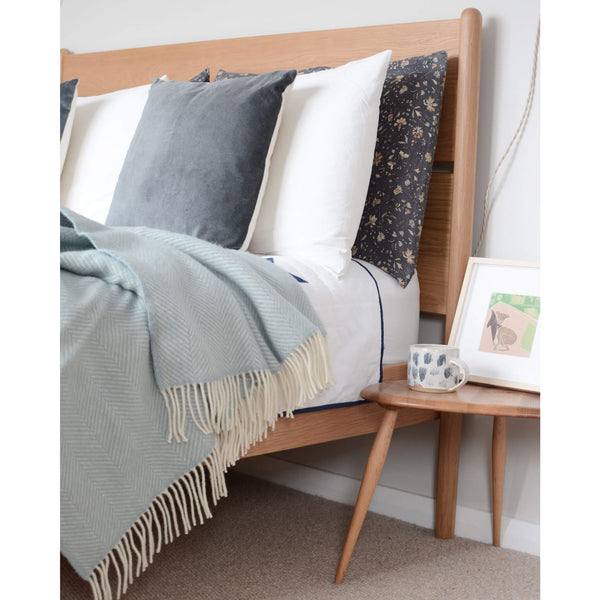 Duck egg blue wool blanket with an ivory fringe. Shown on a bed.