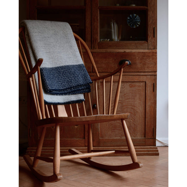 Tweedmill light grey and navy cross weave wool throw, folded on the back of a wooden Ercol rocking chair.