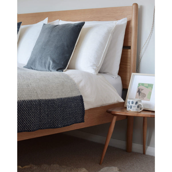 Tweedmill light grey and navy cross weave wool throw, shown on top of a wooden bed.