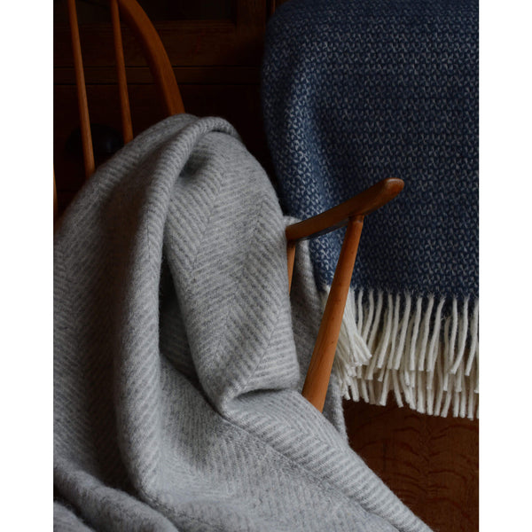 Close up of a Tweedmill pale grey wool throw with a herringbone pattern and ivory fringe.