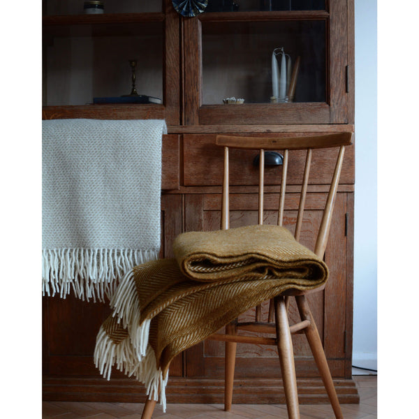Tweedmill oatmeal beehive wool throw shown infront of a wooden cabinet.