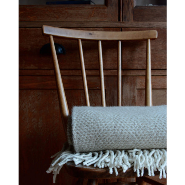 Tweedmill oatmeal beehive wool throw, folded on top of a wooden dining chair.