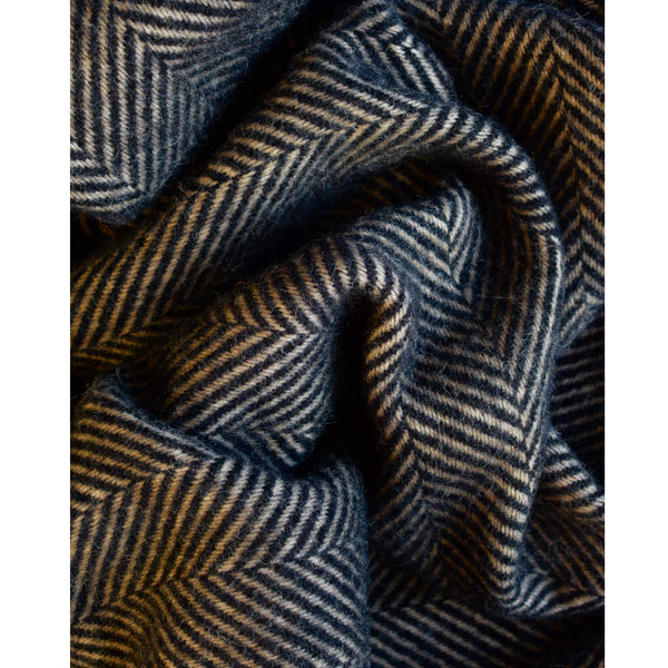 A close up of a dark brown wool throw with a herringbone pattern and fringe, shown on a parquet floor.