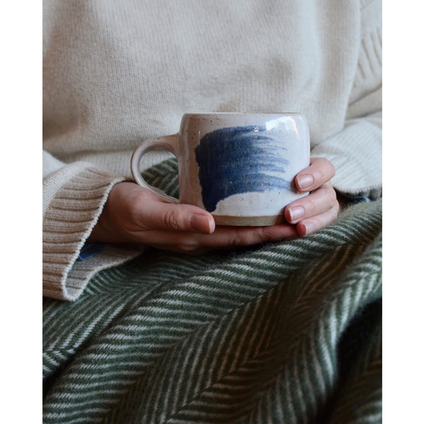 An olive green Tweedmill herringbone wool throw, draped over a woman's lap.