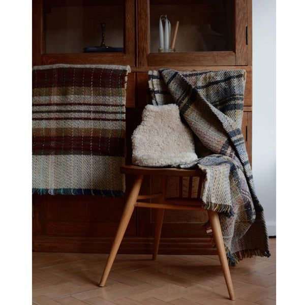Recycled wool Tweedmill blankets shown with a sheepskin hot water bottle, in front of a vintage wooden cabinet.