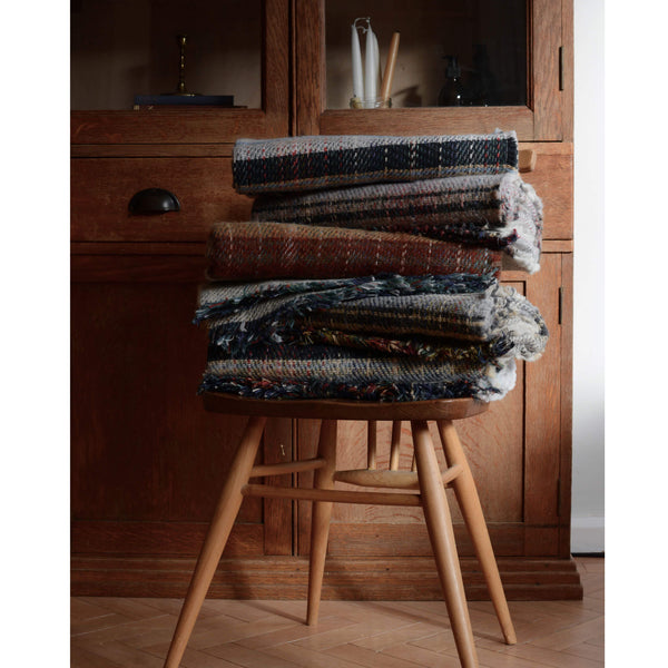 A pile of folded recycled wool blankets, shown in front of a vintage wooden cabinet.