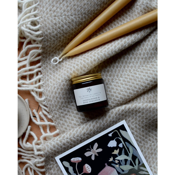 Sandalwood and Rose Geranium scented candle by The Botanical candle co. On a blanket with beeswax candles.