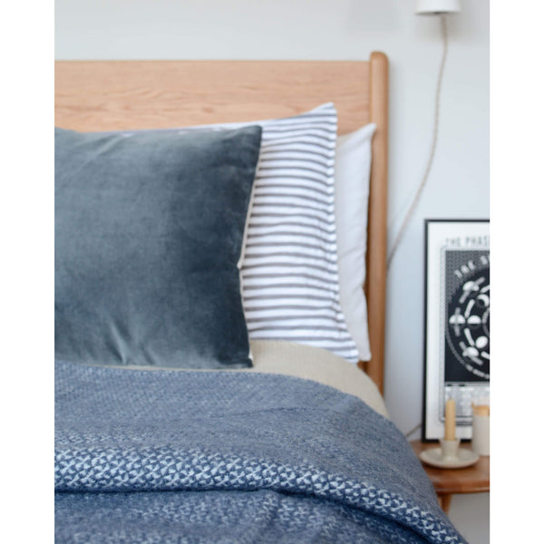 A blue windmill design wool throw, shown draped across a styled bed.