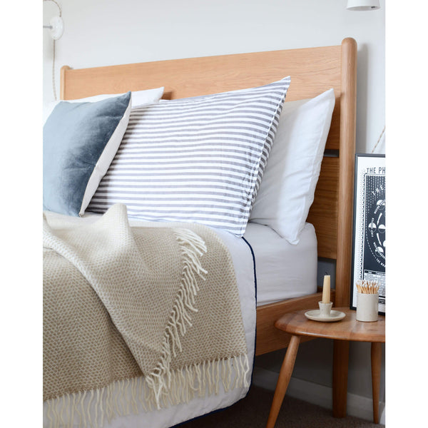 An oatmeal beehive wool throw, shown draped across a styled bed.
