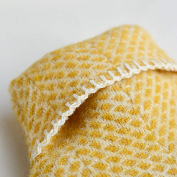 A close up of a  bright yellow wool hot water bottle with a beehive pattern, on a white background.